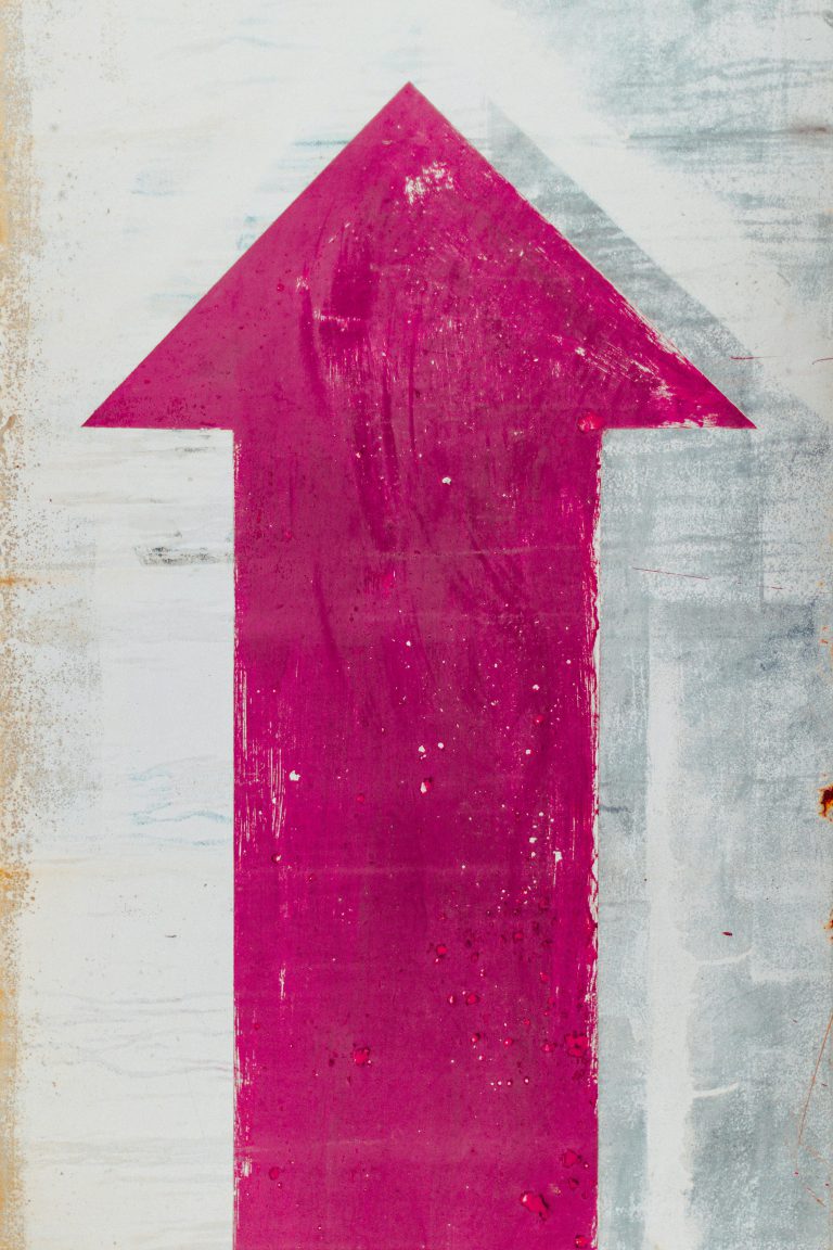 Close-up of a painted pink arrow on a worn-out textured wall in Málaga.