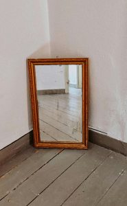 Mentoring Rustic mirror leaning against wall reflecting vintage wooden floor and open door.