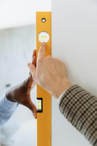 Mentoring Close-up of hands using a yellow bubble level on a white wall indoors, checking alignment.