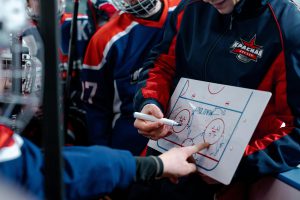 Über Mich Hockey coach discussing tactics on a board with players during match break.